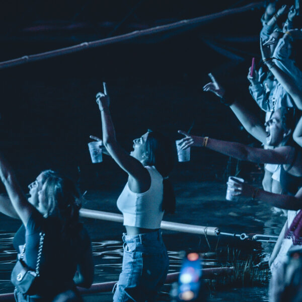 Grupo de asistentes bailando y levantando los brazos junto al agua en un concierto nocturno del Festival Pirineos Sur.