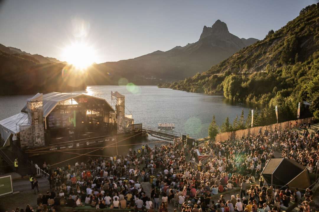 Concierto en el escenario flotante de Pirineos Sur al atardecer con el sol ocultándose tras las montañas.
